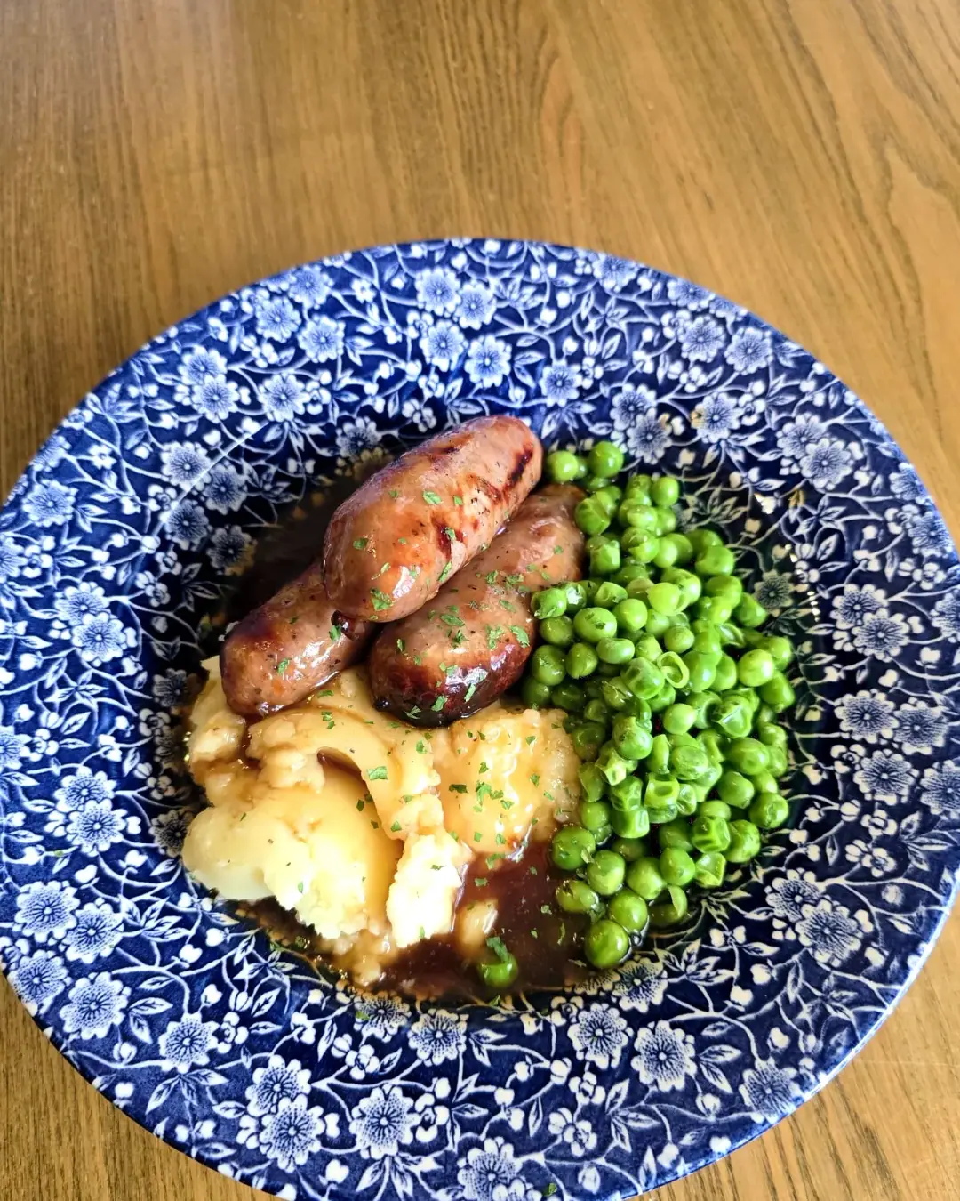 Sausages and mash with gravy and peas on a blue willow-pattern plate