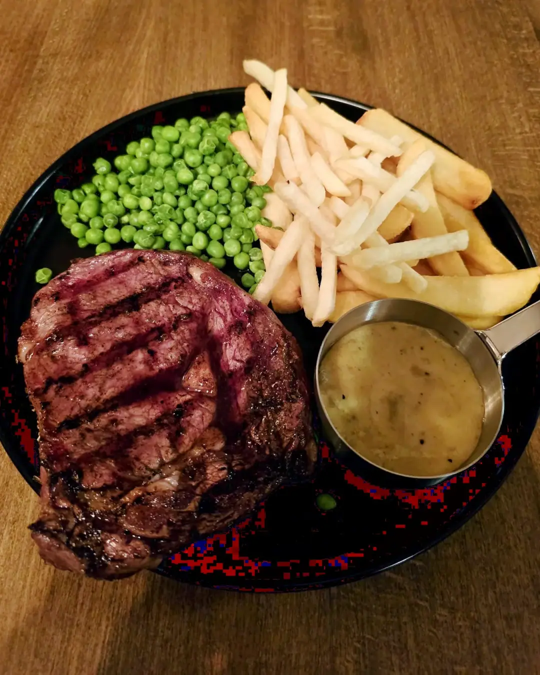 Chargrilled ribeye steak with chips, peas and peppercorn sauce