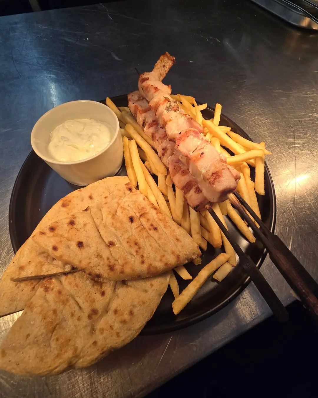 Chicken souvlaki skewers on fries, with grilled pitta and tzatziki