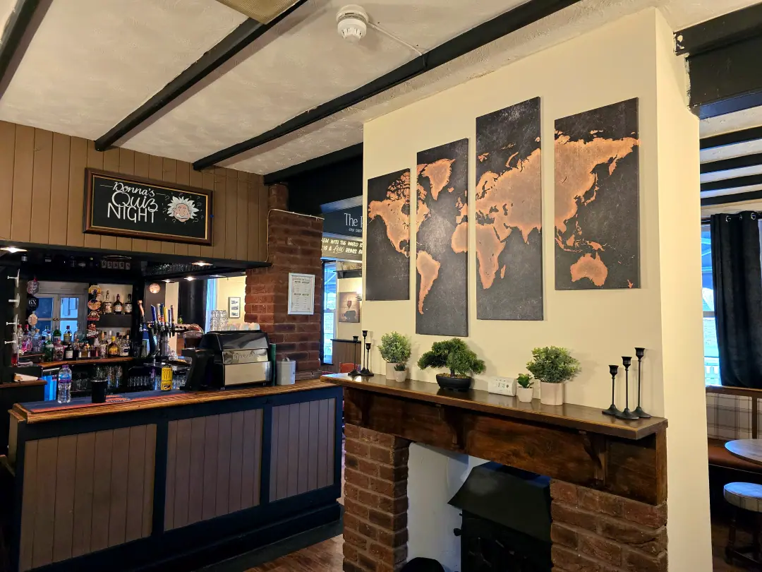 The bar on quiz night, with the quiz board above the counter and a brick fireplace under a map of the world